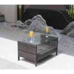 Outdoor coffee table with clear tempered glass top and brown PE rattan frame on a patio