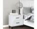 Minimalist bedside table in white with two drawers, next to a bed with soft lighting