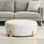 Goldoma white fabric footrest stool with splayed rubber wood legs in a living room near a sofa
