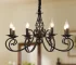 8-light rustic candle chandelier in black iron, hanging above a farmhouse kitchen island with pendant lights.