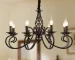 8-light rustic candle chandelier in black iron, hanging above a farmhouse kitchen island with pendant lights.