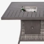 Gray wicker outdoor gas fire pit table with ice bucket and glass wind guard on patio