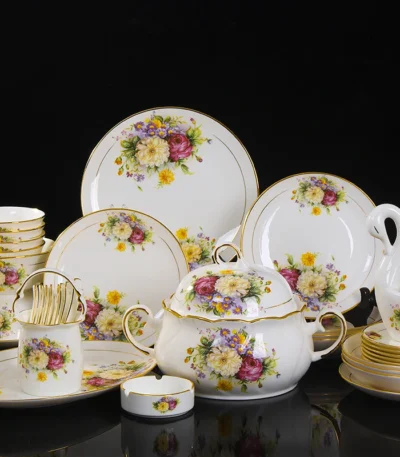 Elegant bone china dinnerware set with plates, bowls, and soup spoons on a wooden table