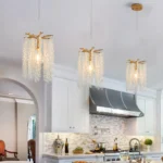 Three-pack golden waterfall pendant lights hanging in a row over a modern kitchen island, crystals sparkling.
