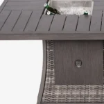 Gray wicker outdoor gas fire pit table with ice bucket and glass wind guard on patio
