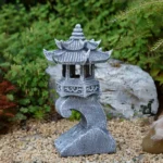 Side view of stone palace lantern with tiered roof and intricate carvings, in a rock garden.