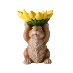 Bird feeder bunny statue viewed from behind, tail and hat visible, on grass.