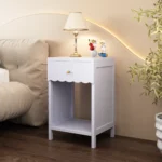 Modern nightstand with scalloped edge drawer and open shelf in lilac color, placed beside a bed