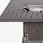 Gray wicker outdoor gas fire pit table with ice bucket and glass wind guard on patio