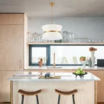 Modern chandelier with white fabric shade and brass finish hanging over kitchen island