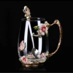Elegant crystal glass tea mug with enamel floral design and handgrip on a wooden table