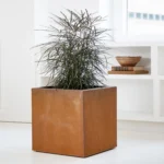Retro corten steel cube planter with weathered orange-brown patina, placed on a modern patio with greenery.