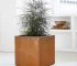 Large metal cube planter in corten steel placed in a modern garden with lush greenery