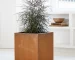 Large metal cube planter in corten steel placed in a modern garden with lush greenery
