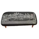Goldoma 38-inch black wool ottoman with brown legs and nailhead trim used as a stylish footrest in a modern living room