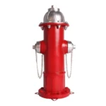 Front view of fire hydrant statue, bright red color against green hedge.
