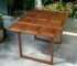 Brown solid wood outdoor dining table with foldable legs on a patio