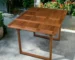 Brown solid wood outdoor dining table with foldable legs on a patio