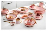 Elegant dinnerware set with gilt rim pink porcelain plates, bowls, mugs, and cutlery on a table