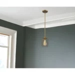 Close-up of the brushed gold metal cage of the HMS hanging light, showing the warm glow of the 3000K LED bulb through