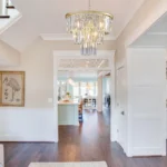 The 7-light chandelier hanging in a bright entryway, with natural light reflecting off the crystals and gold frame.