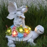 Solar angel garden statue light with resin angel riding a turtle, glowing softly in a flower bed at dusk.