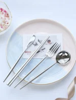 Elegant stainless steel flatware set with forks, spoons, and knives arranged on a wooden table