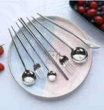 Elegant stainless steel flatware set with forks, spoons, and knives arranged on a wooden table