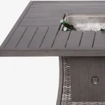 Gray wicker outdoor gas fire pit table with ice bucket and glass wind guard on patio