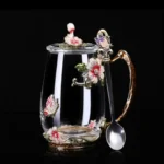 Elegant crystal glass tea mug with enamel floral design and handgrip on a wooden table