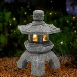 Solar Pagoda Lantern Garden Statue with gray stone finish, placed on a wooden deck surrounded by greenery.