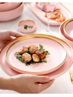 Elegant dinnerware set with gilt rim pink porcelain plates, bowls, mugs, and cutlery on a table