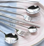 Elegant stainless steel flatware set with forks, spoons, and knives arranged on a wooden table