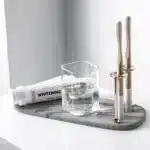Toothbrush holder with a transparent base and stainless steel accents on a wooden shelf.