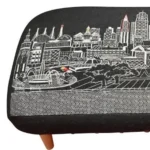 Goldoma 38-inch black wool ottoman with brown legs and nailhead trim used as a stylish footrest in a modern living room
