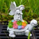 The outdoor angel and turtle statue illuminated at night, casting a warm glow on the garden ground.