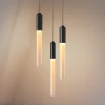 Modern LED long pendant light in warm acrylic, hanging above a wooden dining table in a restaurant setting.
