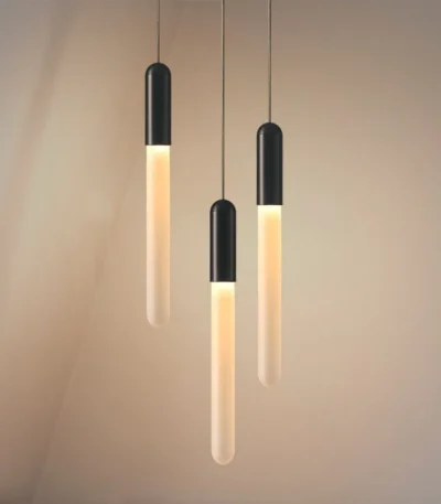 Modern LED long pendant light in warm acrylic, hanging above a wooden dining table in a restaurant setting.