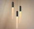 Modern LED long pendant light in warm acrylic, hanging above a wooden dining table in a restaurant setting.