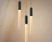 Modern LED long pendant light in warm acrylic, hanging above a wooden dining table in a restaurant setting.