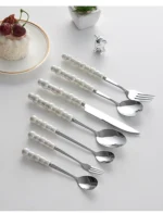 Stainless steel flatware set with ceramic pearl handles on wooden table