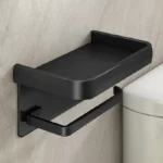Aluminum toilet paper holder with shelf holding a candle and small vase, warm lighting.