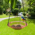 Bird bath and feeder combo with a blue bowl, hanging near a flowering bush in a garden.
