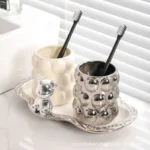 Pair of electroplated ceramic mugs with toothbrush slots, placed on a wooden bathroom shelf.