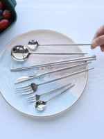 Elegant stainless steel flatware set with forks, spoons, and knives arranged on a wooden table