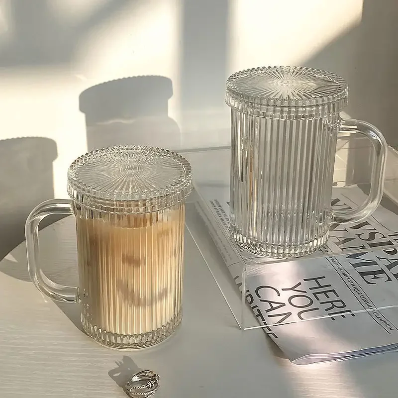 Set of transparent glass coffee mugs with lids and straws on a wooden table