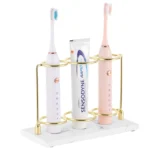 White resin electric toothbrush holder with 3 slots on a marble bathroom countertop.