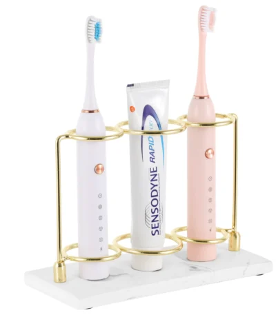 White resin electric toothbrush holder with 3 slots on a marble bathroom countertop.