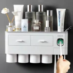 White magnetic toothbrush holder with toothpaste dispenser and cup, mounted on bathroom tile wall.