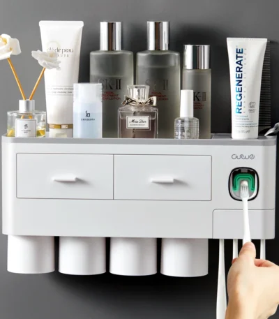 White magnetic toothbrush holder with toothpaste dispenser and cup, mounted on bathroom tile wall.